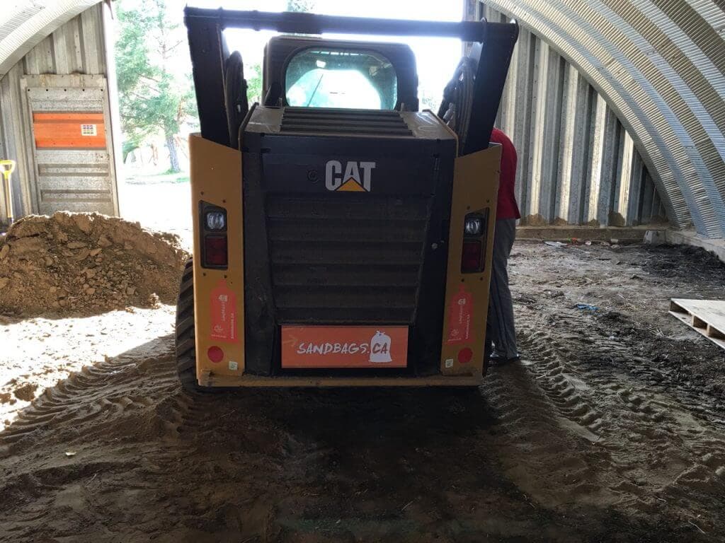 Skid steer inside the sandbag filling shed with a pile of sand